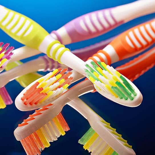 Colorful toothbrushes arranged in circle on blue background, displaying dental hygiene products.