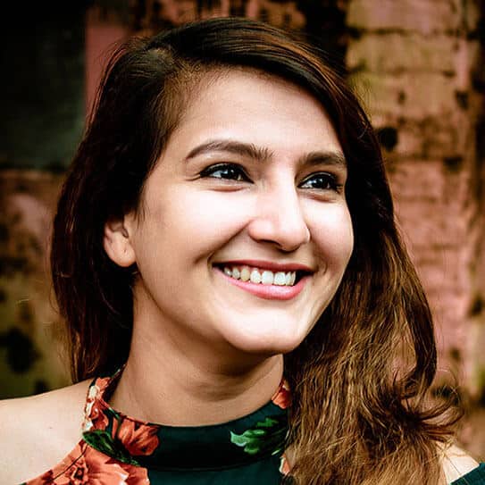Smiling woman with dark hair against brick wall background, professional headshot for dental practice.
