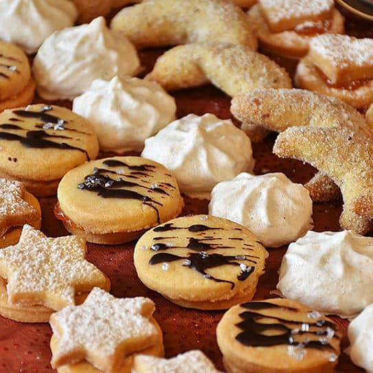 Assorted decorated cookies including star-shaped, white meringue, and chocolate-drizzled varieties on red surface.