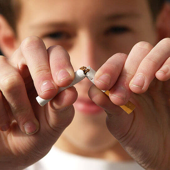 Child breaking cigarette in half against blurred background, symbolizing smoking cessation and health awareness.