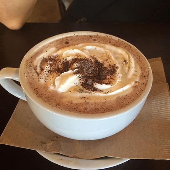 Cappuccino with cocoa powder and latte art in white cup on brown napkin