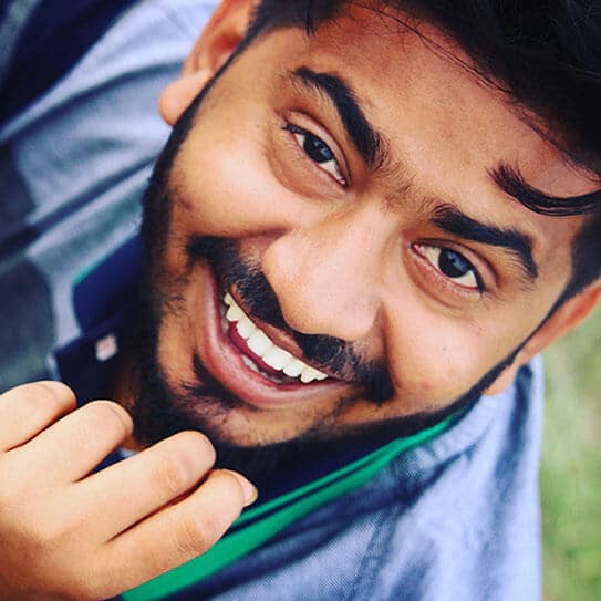 Young man smiling brightly outdoors, wearing blue shirt, promoting dental health and wellness.