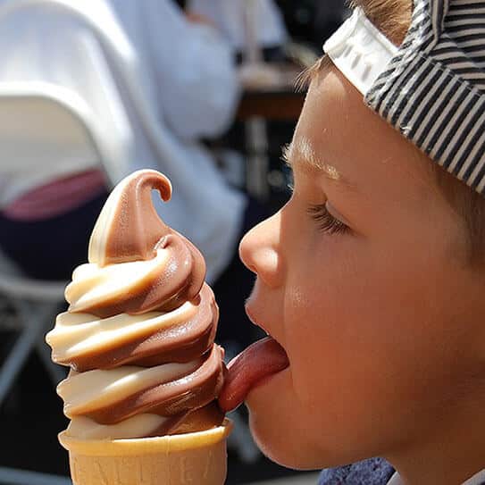 Child eating swirl ice cream cone outdoors during daytime.