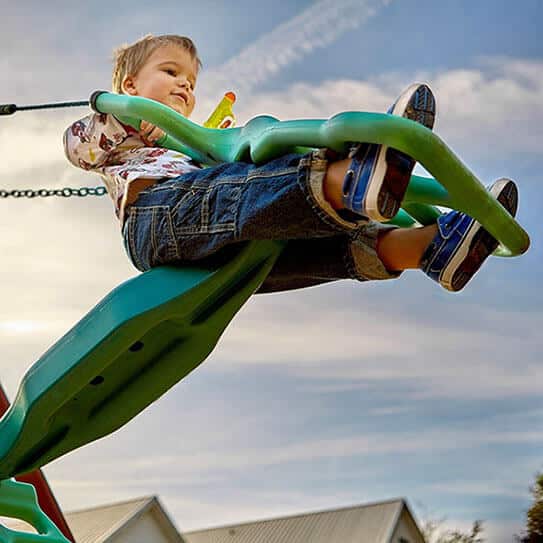 Young child flying on green airplane ride against blue sky outdoors.