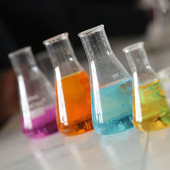 Five test tubes containing colorful liquids in pink, orange, blue, and yellow arranged in a row.