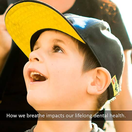 Young child wearing yellow and black cap looking upward, illustrating breathing's impact on dental health.