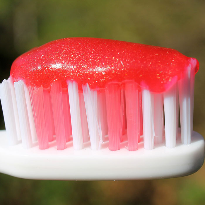 Toothbrush with red toothpaste blob on white bristles against blurred background.