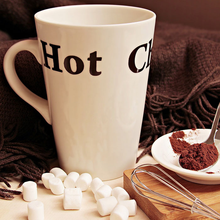 tooth-sensitivity-2022_700.jpg White mug with "Hot C" text surrounded by marshmallows, chocolate, and cozy blanket setup.
