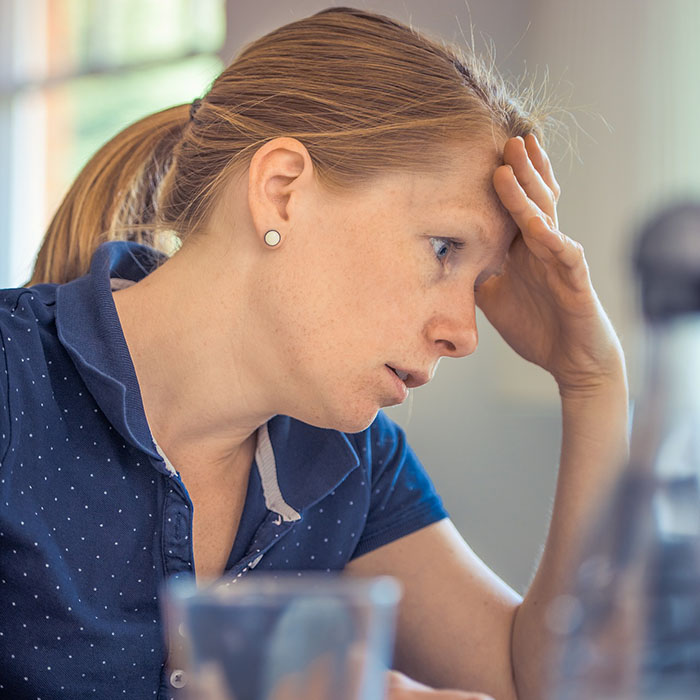 oral-health-stress-2022_700.jpg Woman in blue shirt with hand to head, appearing stressed or thoughtful in office setting.