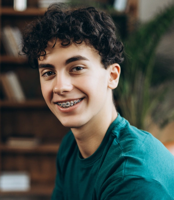 A teenage boy with metal braces smiling confidently at Denver Orthodontics and Dental Lounge in Denver CO