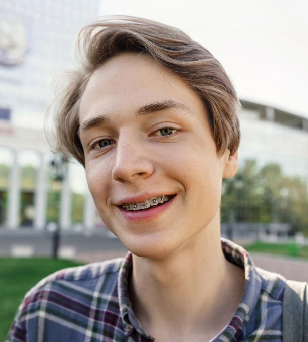 A teenage boy smiling confidently outdoors after orthodontic treatment at Denver Orthodontics and Dental Lounge in Denver CO