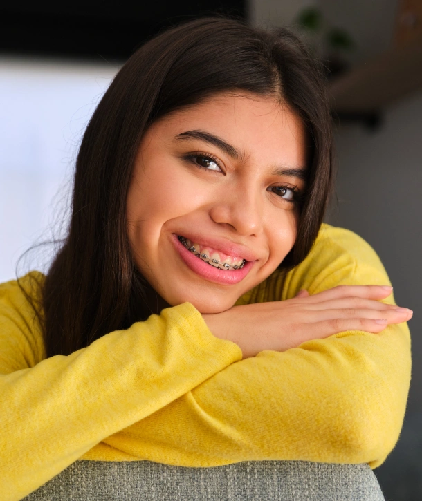 A happy young woman in a yellow top smiling after getting braces at Denver Orthodontics and Dental Lounge in Denver CO