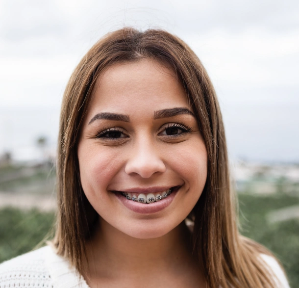 A teenage girl with braces smiling outdoors as a patient of Denver Orthodontics and Dental Lounge in Denver CO