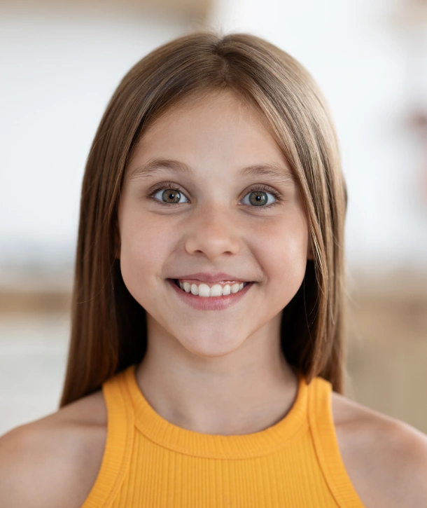 A teenage girl in a yellow top smiling after orthodontic treatment at Denver Orthodontics and Dental Lounge in Denver CO