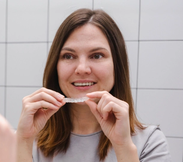 A teenage girl holding a clear aligner and smiling at Denver Orthodontics and Dental Lounge in Denver CO