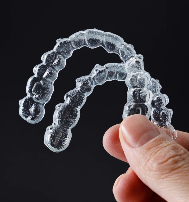 A hand holding a single clear orthodontic aligner at Denver Orthodontics and Dental Lounge in Denver CO