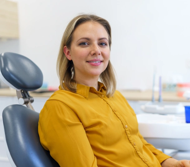 A woman in a yellow top smiling while seated in a dental chair at Denver Orthodontics and Dental Lounge in Denver CO