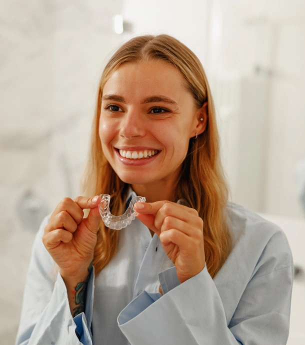 A close up of a woman holding a clear aligner near her mouth at Denver Orthodontics and Dental Lounge in Denver CO