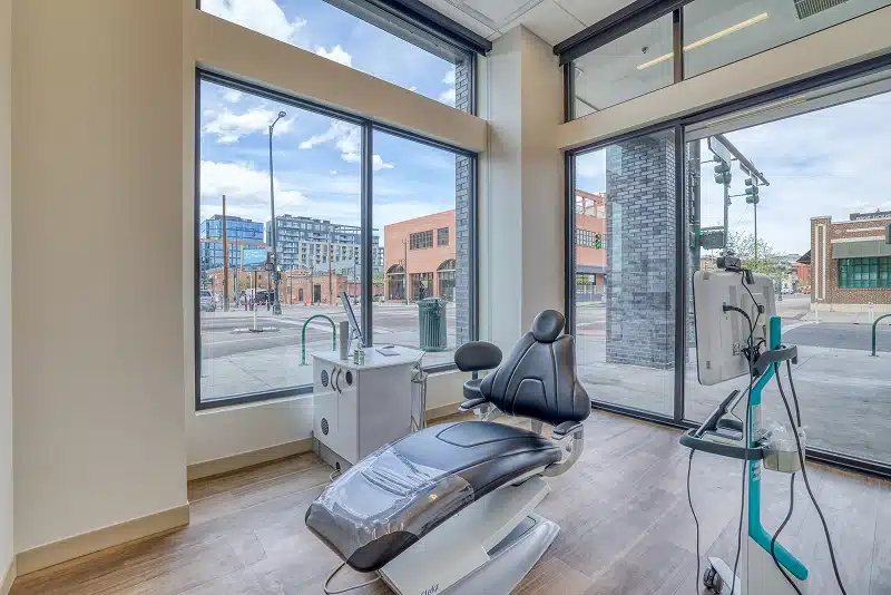 A modern treatment room with a dental chair and floor to ceiling windows overlooking the street at Denver Orthodontics and Dental Lounge in Denver CO