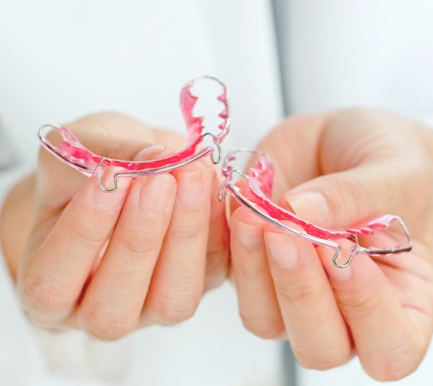 A patient holding two pink Hawley retainers at Denver Orthodontics and Dental Lounge in Denver CO