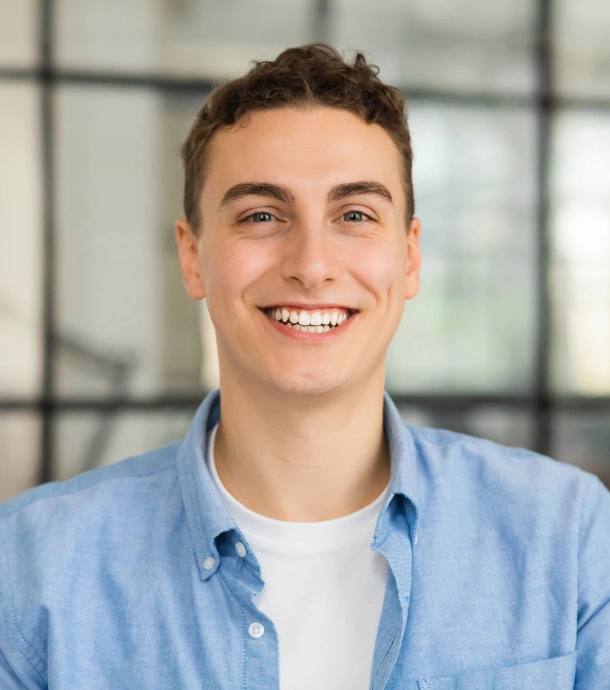 A young man in a blue shirt smiling confidently after orthodontic treatment at Denver Orthodontics and Dental Lounge