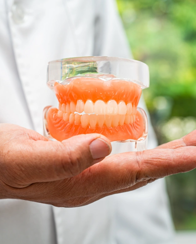 Dentist holding clear denture model with orange gum-colored acrylic material.