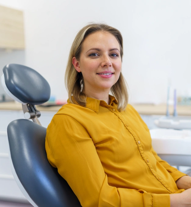Smiling woman in yellow shirt sitting in dental chair during fluoride treatment consultation.