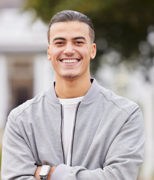 Smiling young man in casual gray jacket outdoors at dental practice.