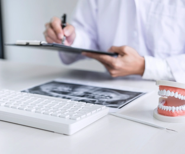 Dentist reviewing dental X-ray with clipboard and tooth model on desk.