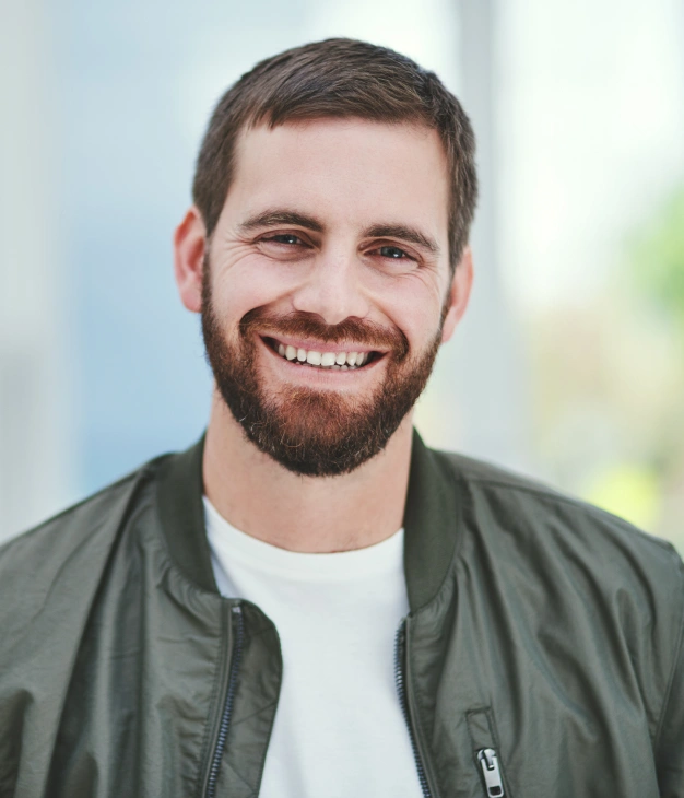 Smiling man with beard wearing olive green jacket for periodontics practice.