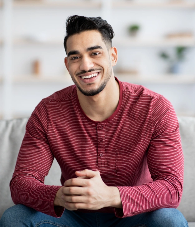 Smiling man in burgundy striped shirt sitting in dental office treatment area.