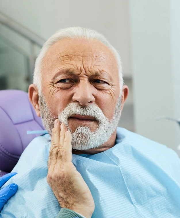 Senior man experiencing tooth pain in a dental office setting.