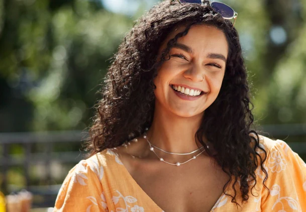 Smiling woman with curly dark hair wearing orange top outdoors in Clewiston.