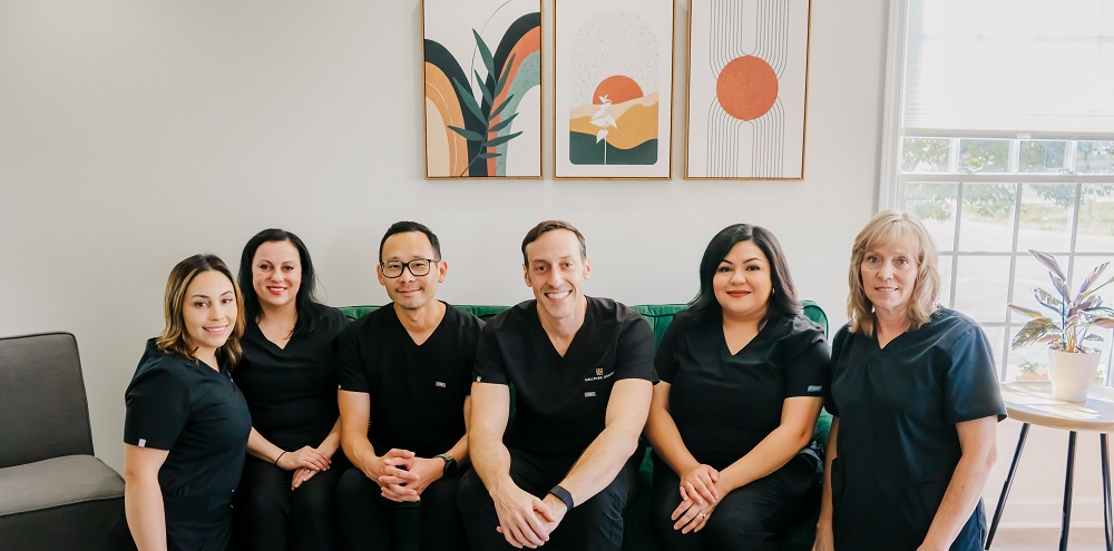 The full dental team with Dr. David Donelson and Dr. Tae Park seated on a sofa at Hallmark Dental in Lewisburg, Tennessee.