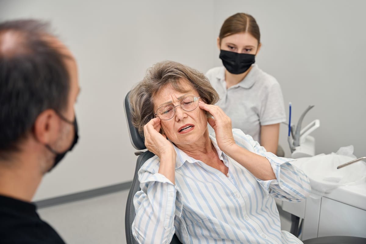 Senior woman experiencing jaw pain during dental consultation with dentist and assistant in Kyle.
