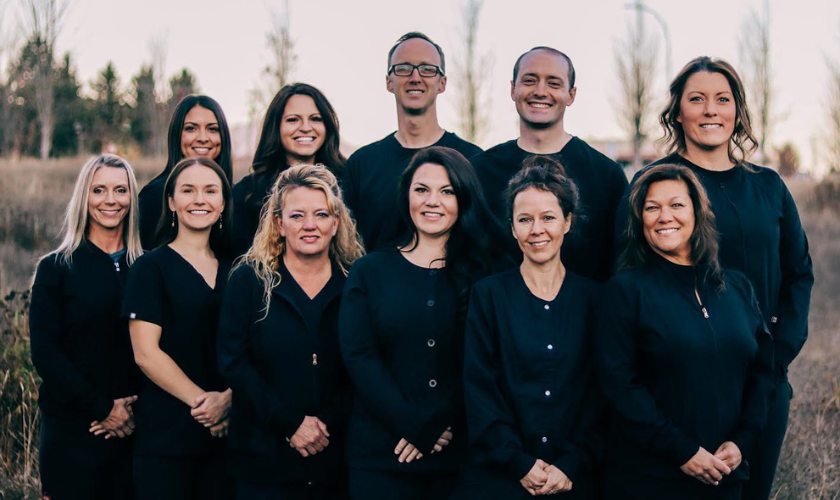 Group of smiling holistic dental team members in dark scrubs