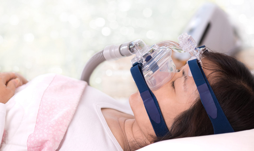 A woman lying down wearing a CPAP mask to treat sleep disordered breathing