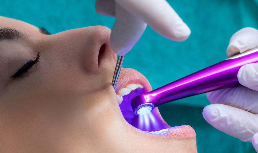 Dentist using a UV light tool near a patient's teeth