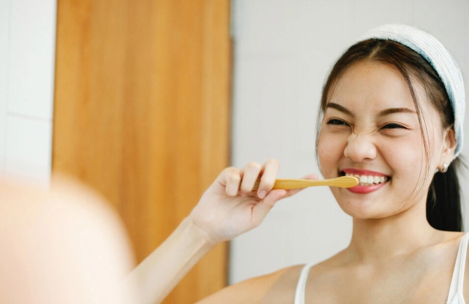 Young woman smiling while brushing her teeth with a bamboo toothbrush in front of a mirror