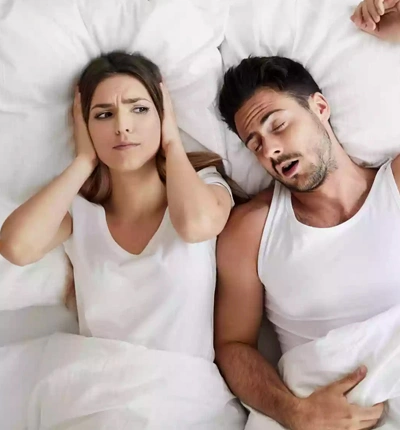 Woman covering her ears while her partner sleeps with his mouth open from sleep apnea