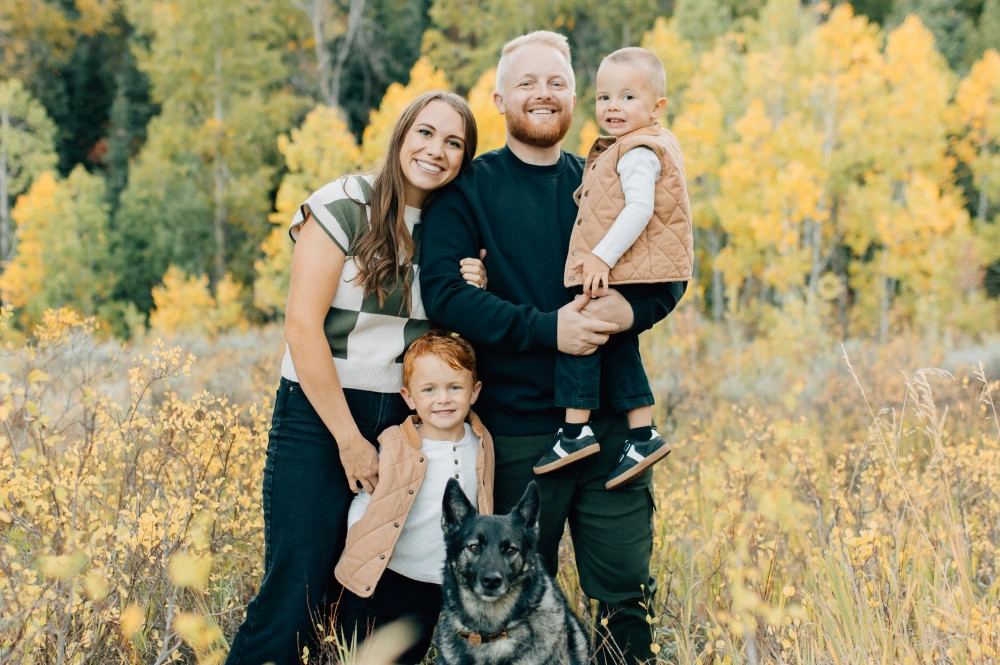 Dr. Dallin Ritchie and his family standing together among autumn yellow trees