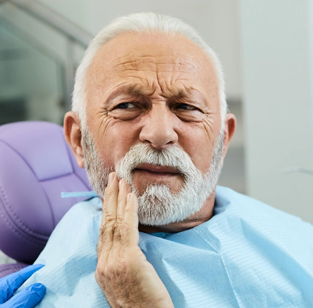 Elderly male patient with beard holding jaw in pain at dental office