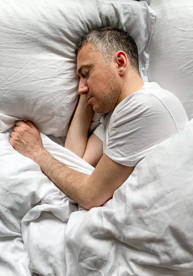 A middle aged man sleeping soundly on his side in a white bed
