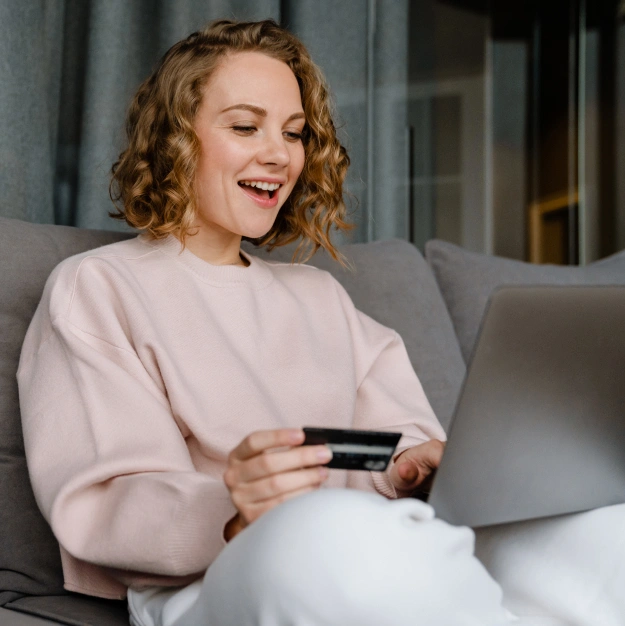 A smiling woman holding a credit card while using a laptop to book an appointment online