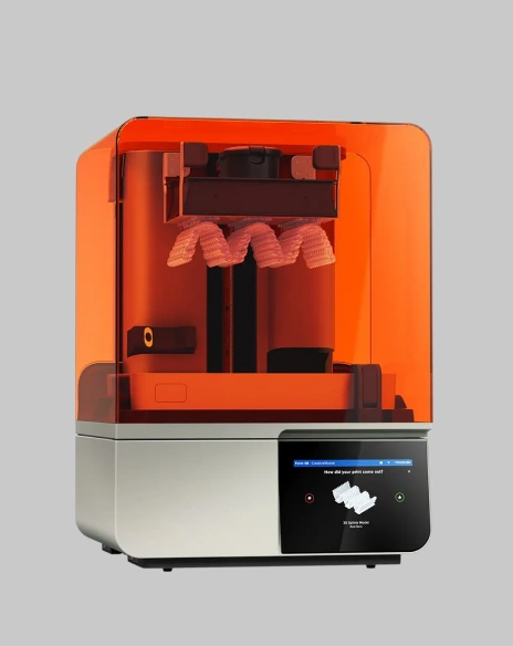 A high-tech digital dental 3D printer with an orange protective cover used for fabricating dental appliances.