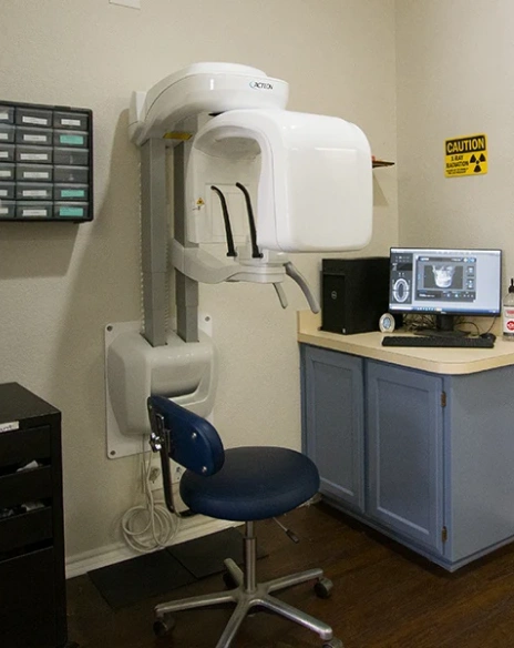 A modern cone beam computed tomography or CBCT 3D dental imaging machine setup in a clinic room next to a computer terminal display.