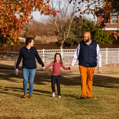 Dr. Talon Davis, his wife, and their daughter holding hands and walking together through a grassy field.