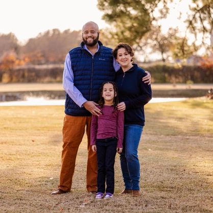 Dr. Talon Davis, his wife, and their daughter posing together outside in a park