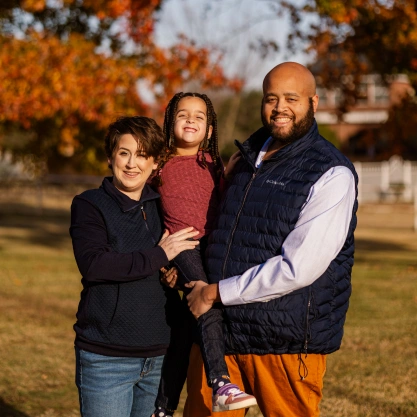 Dr. Talon Davis posing outdoors with his wife and two young daughters for a family portrait.