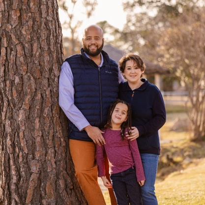 Dr. Davis and his family standing together by a large tree trunk in an outdoor autumn setting.